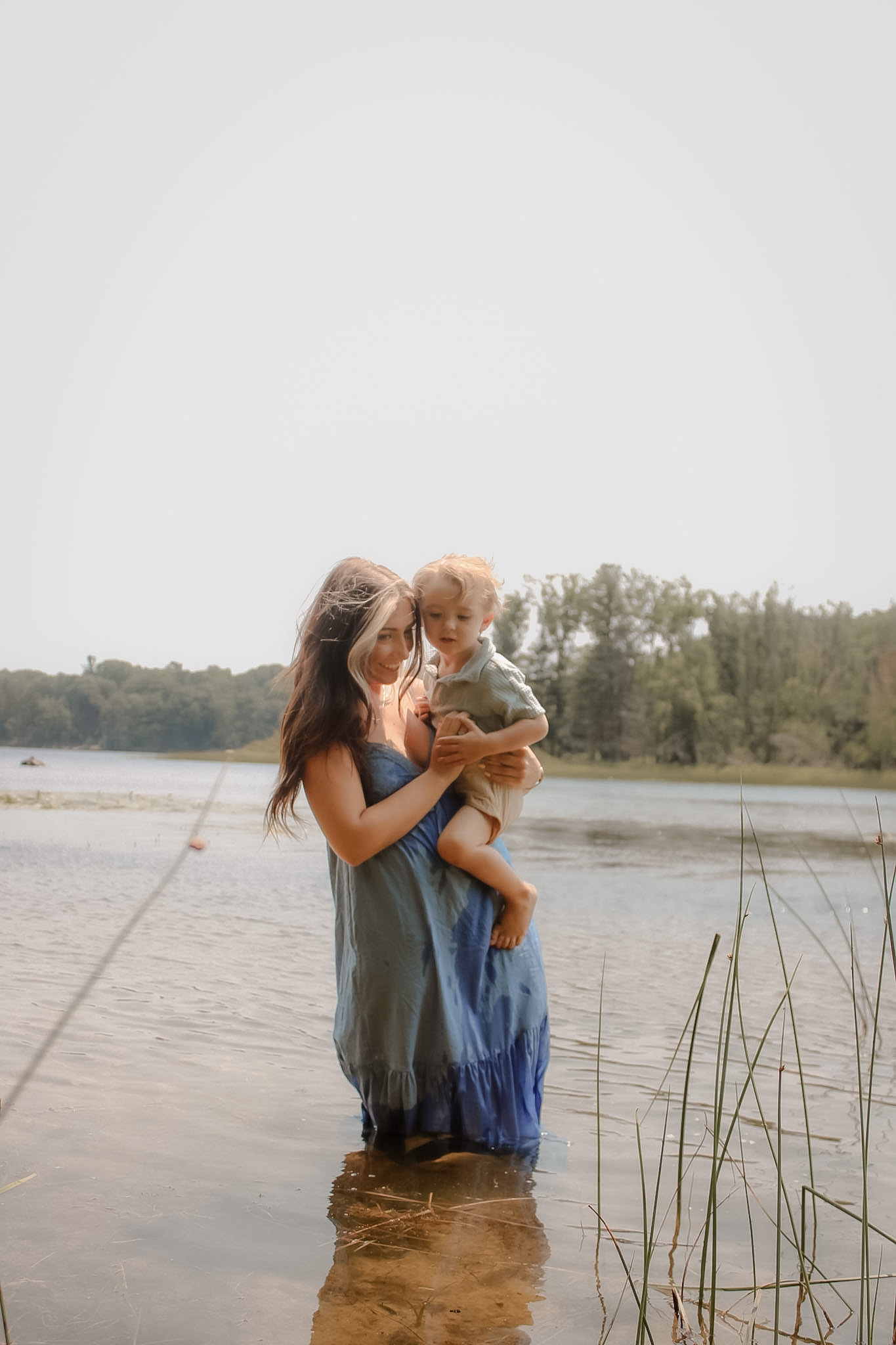Mother holding her young child while standing in shallow lake water