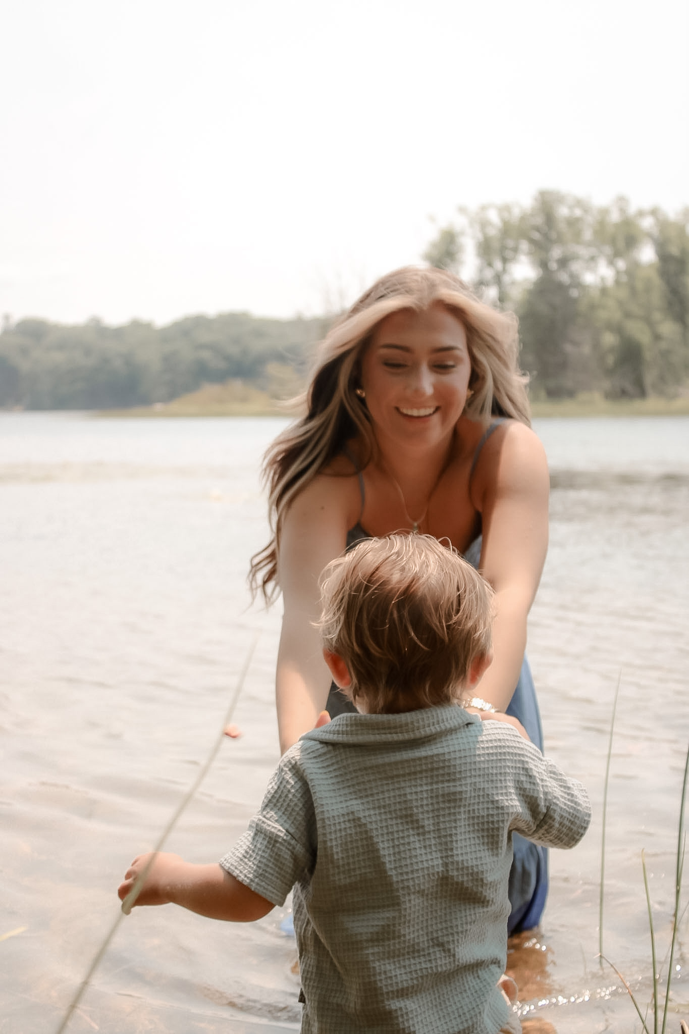 Young child running toward his smiling mother in the shallow lake water