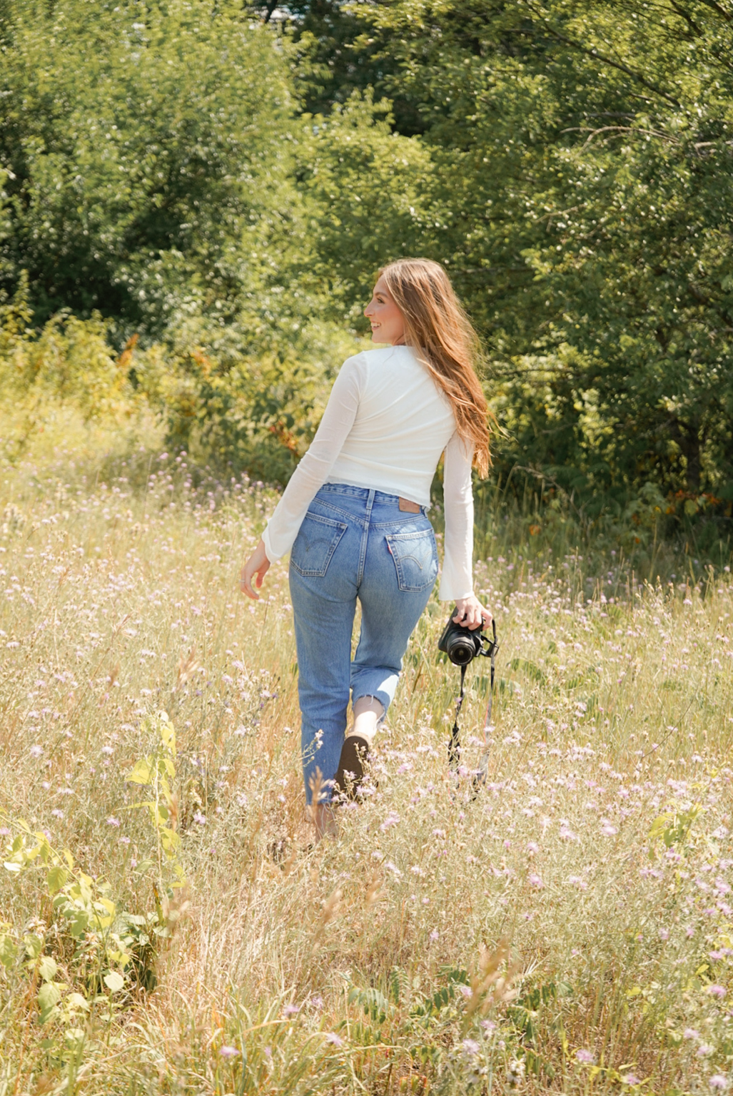 Lexus Erickson holding a camera in a sunlit West Michigan field