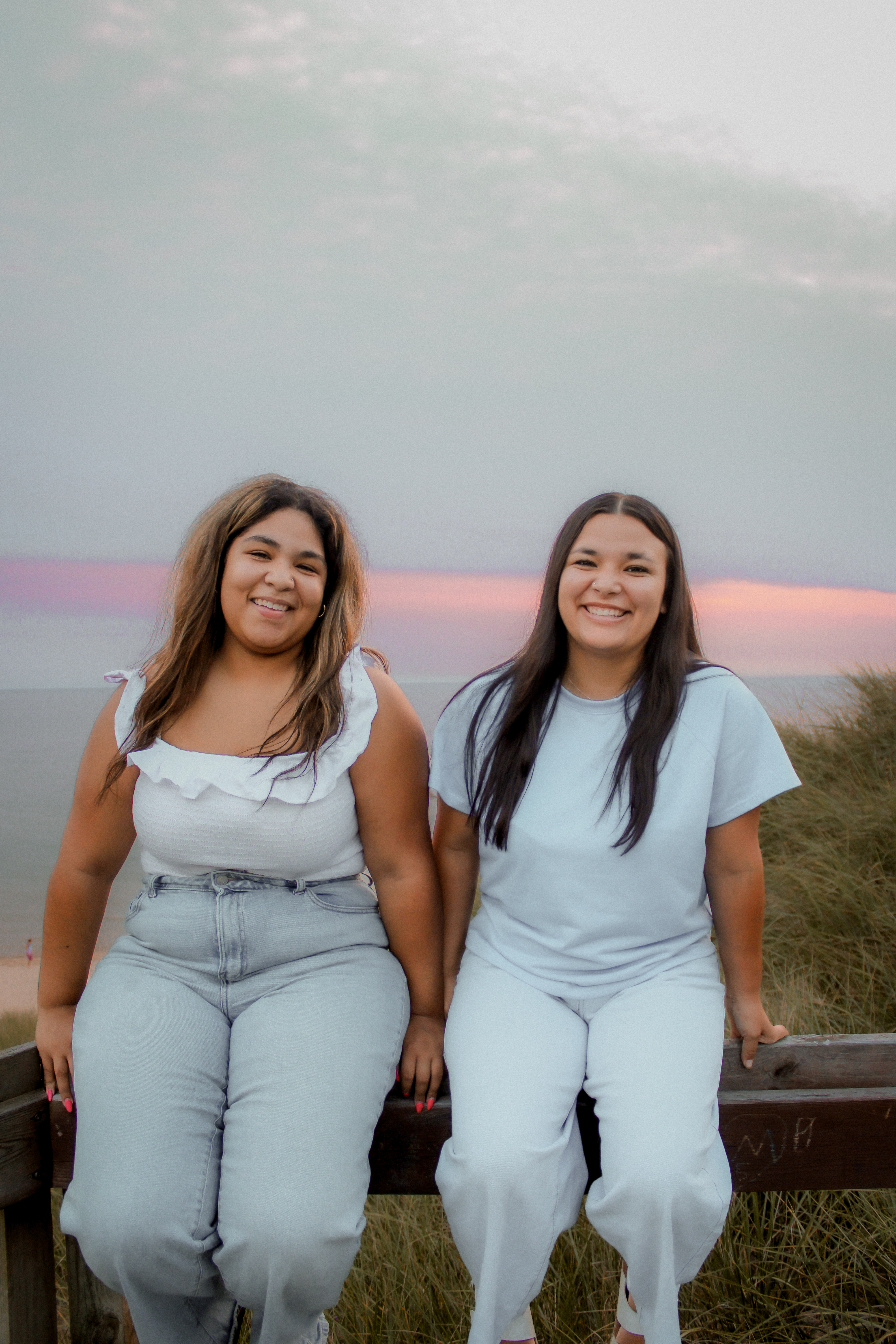 Two best friends seated together outdoors and smiling at the camera