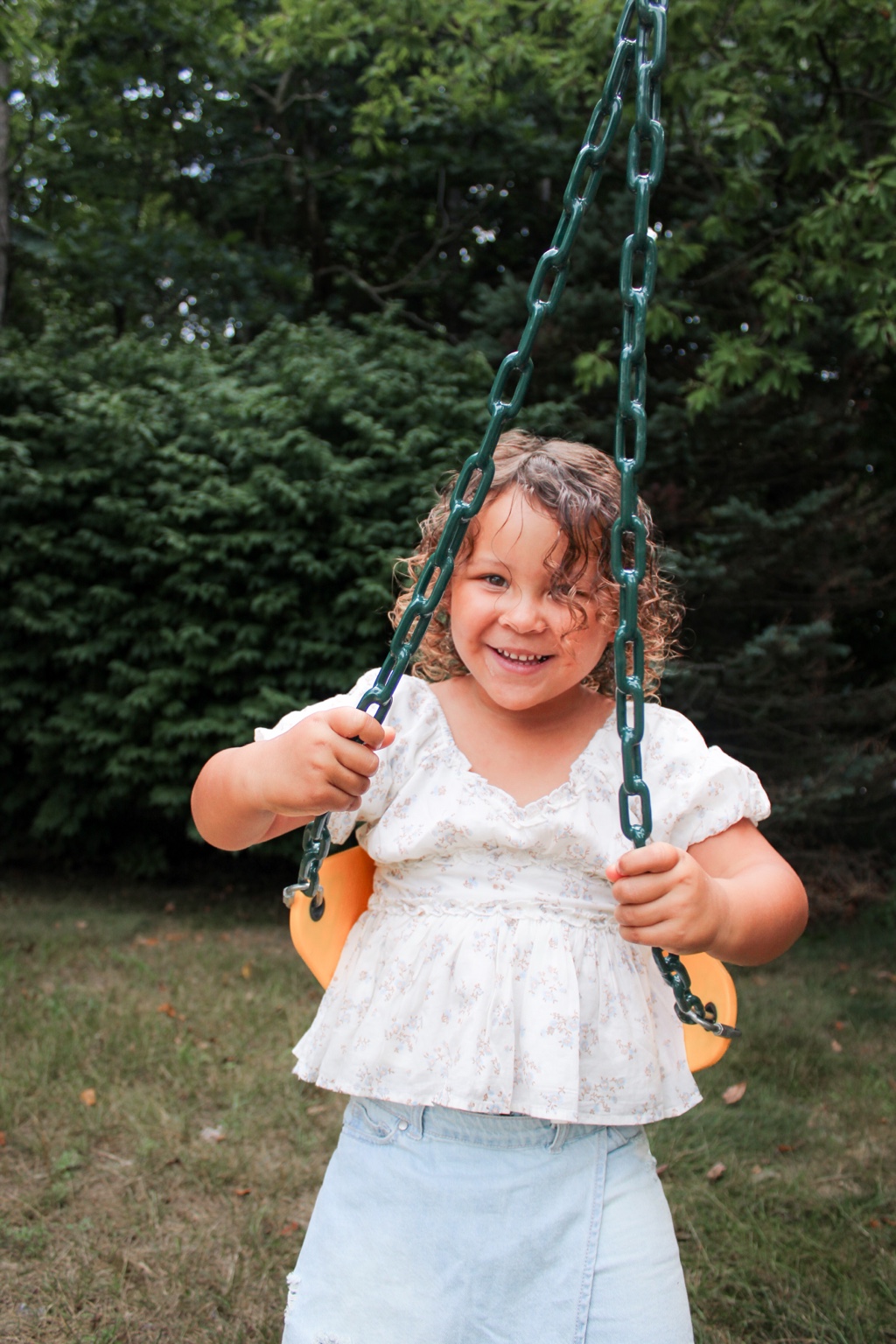 Preschool-aged child smiling while holding the chains of an outdoor swing