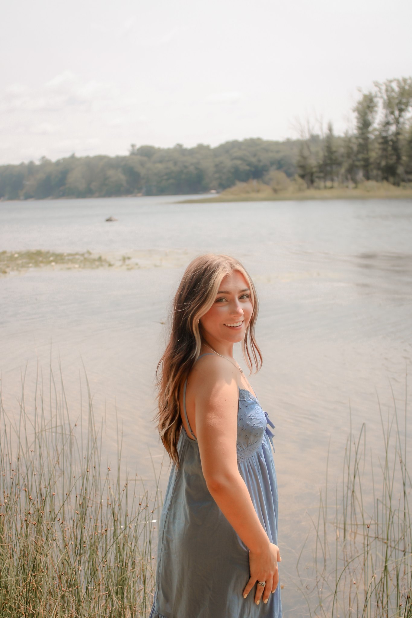 Portrait in a blue dress looking back beside a quiet lake