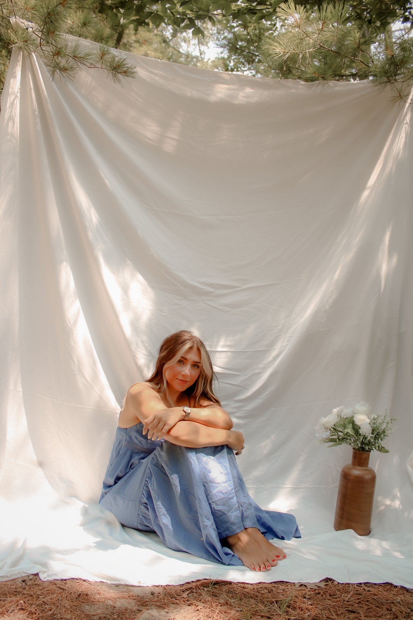 Seated portrait in a blue dress against draped white fabric with flowers