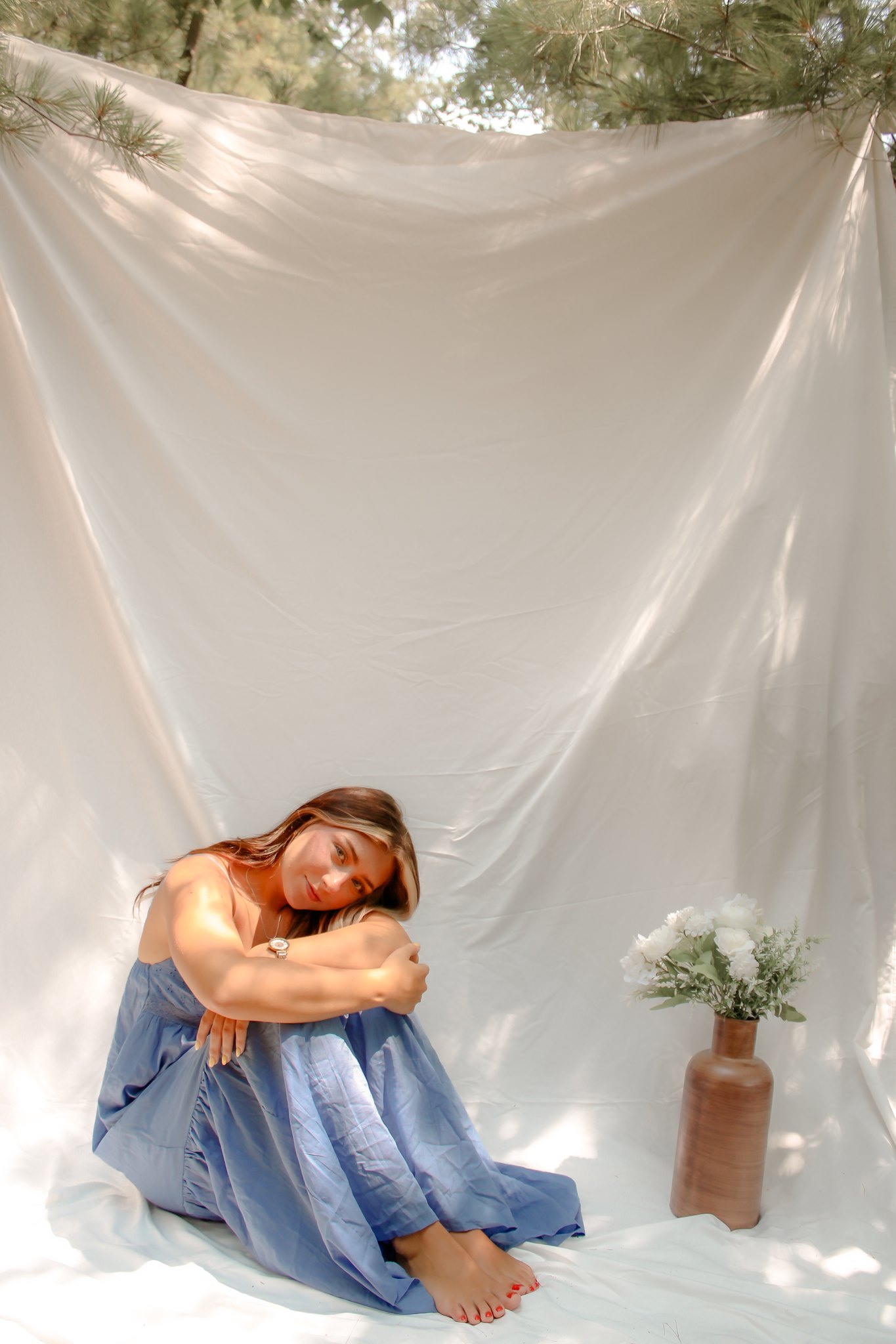 Seated portrait resting her head on folded arms against a soft white backdrop