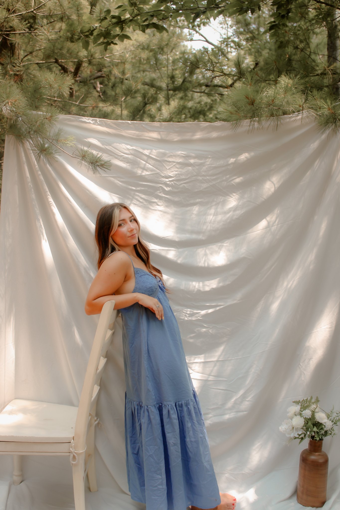 Full-length portrait leaning beside a chair against a draped white backdrop