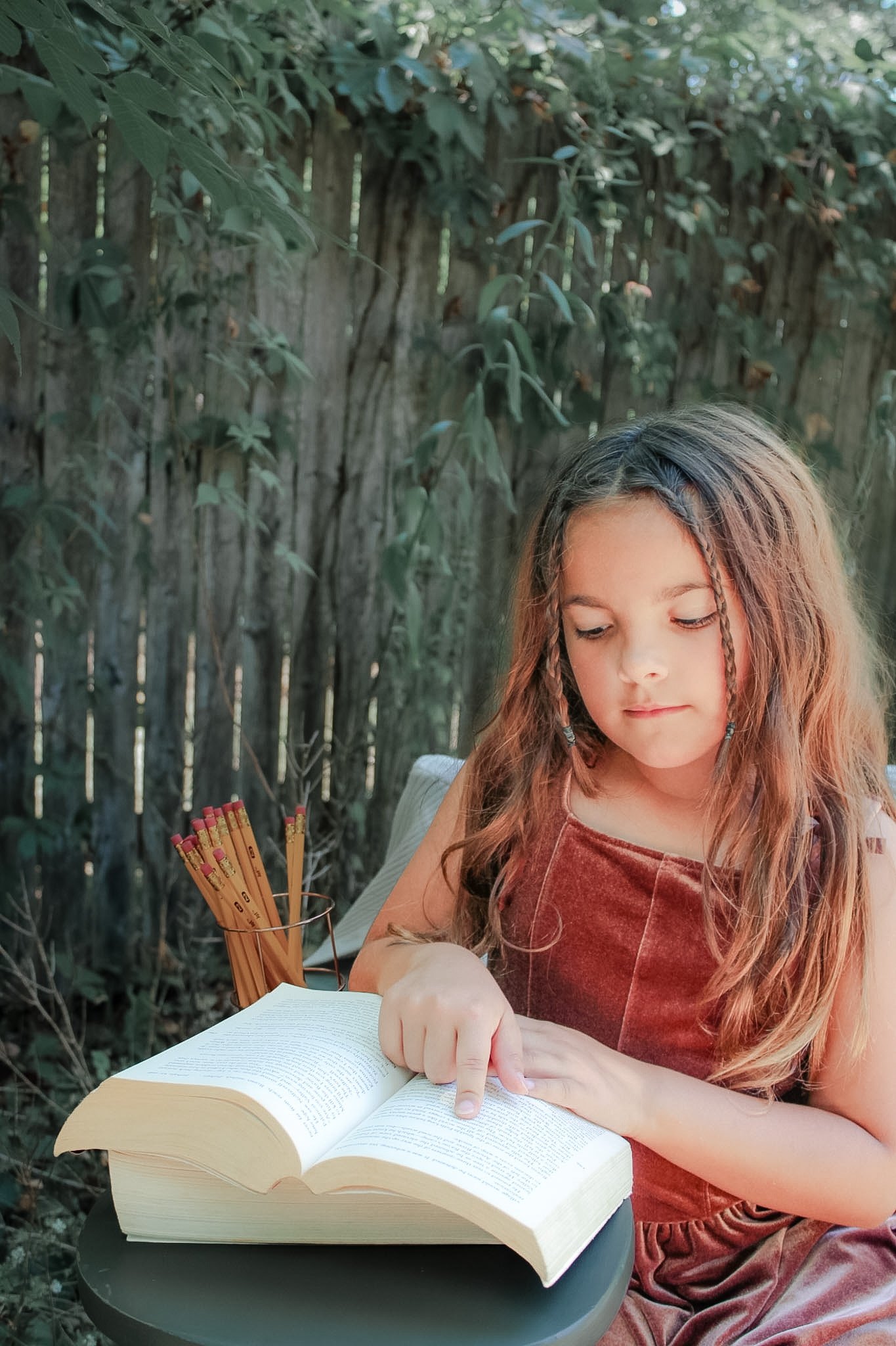 Young student reading an open book beside a cup of pencils