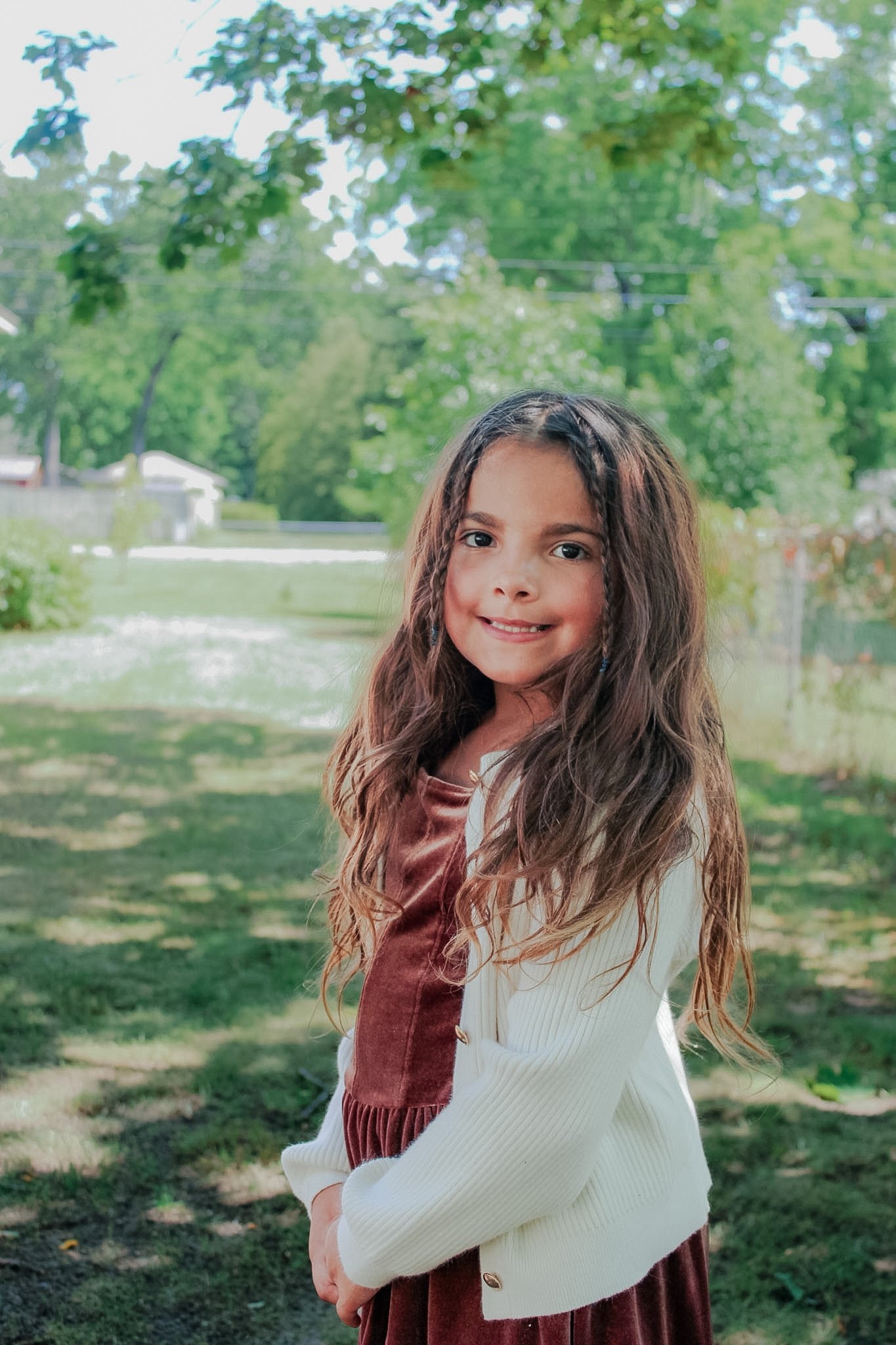 Young student smiling outdoors in a brown dress and cream cardigan